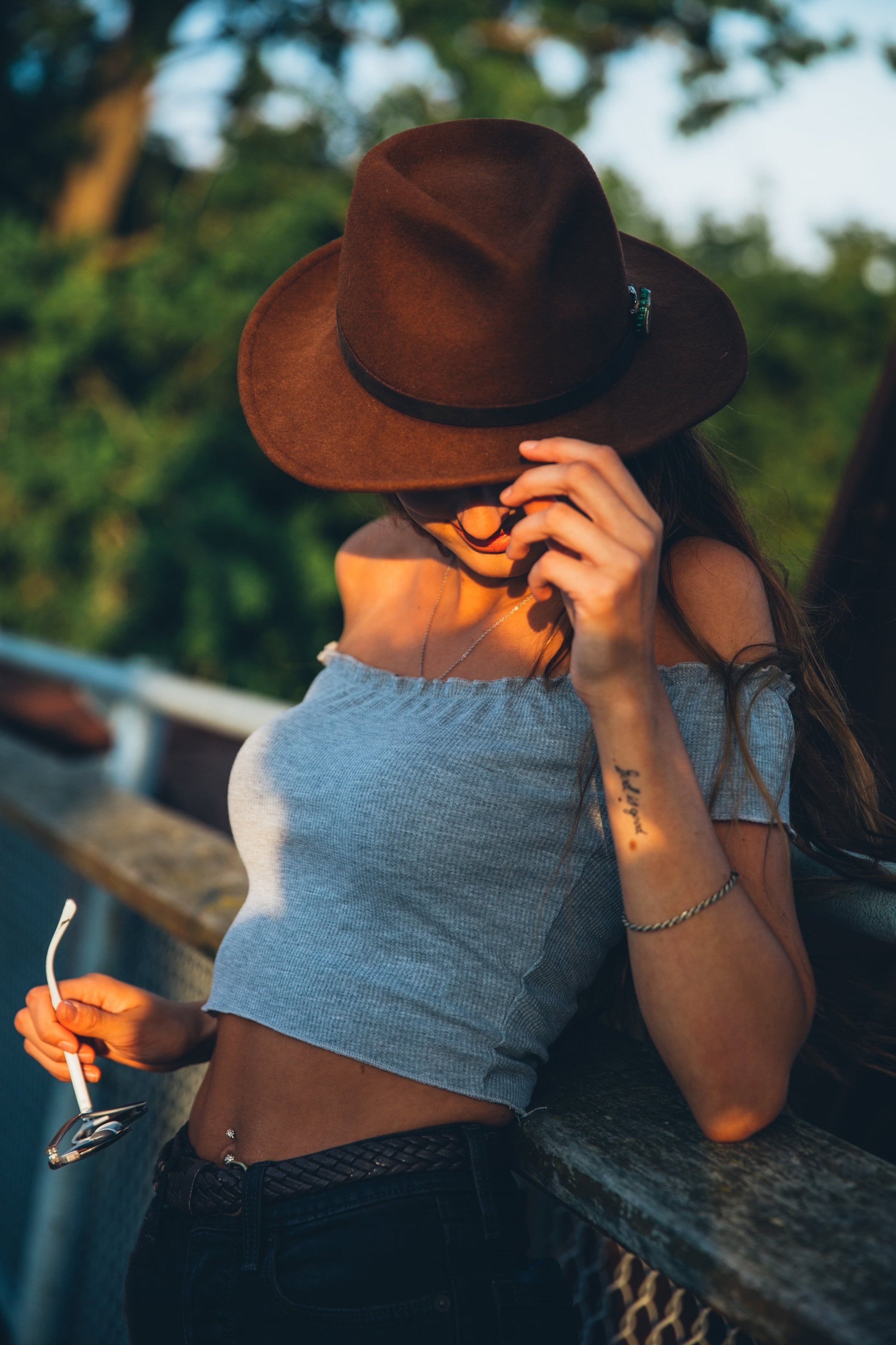 a person posing wearing a grey crop top and a brown hat 