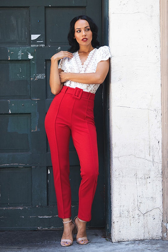 a woman leaning against a wall wearing red pants